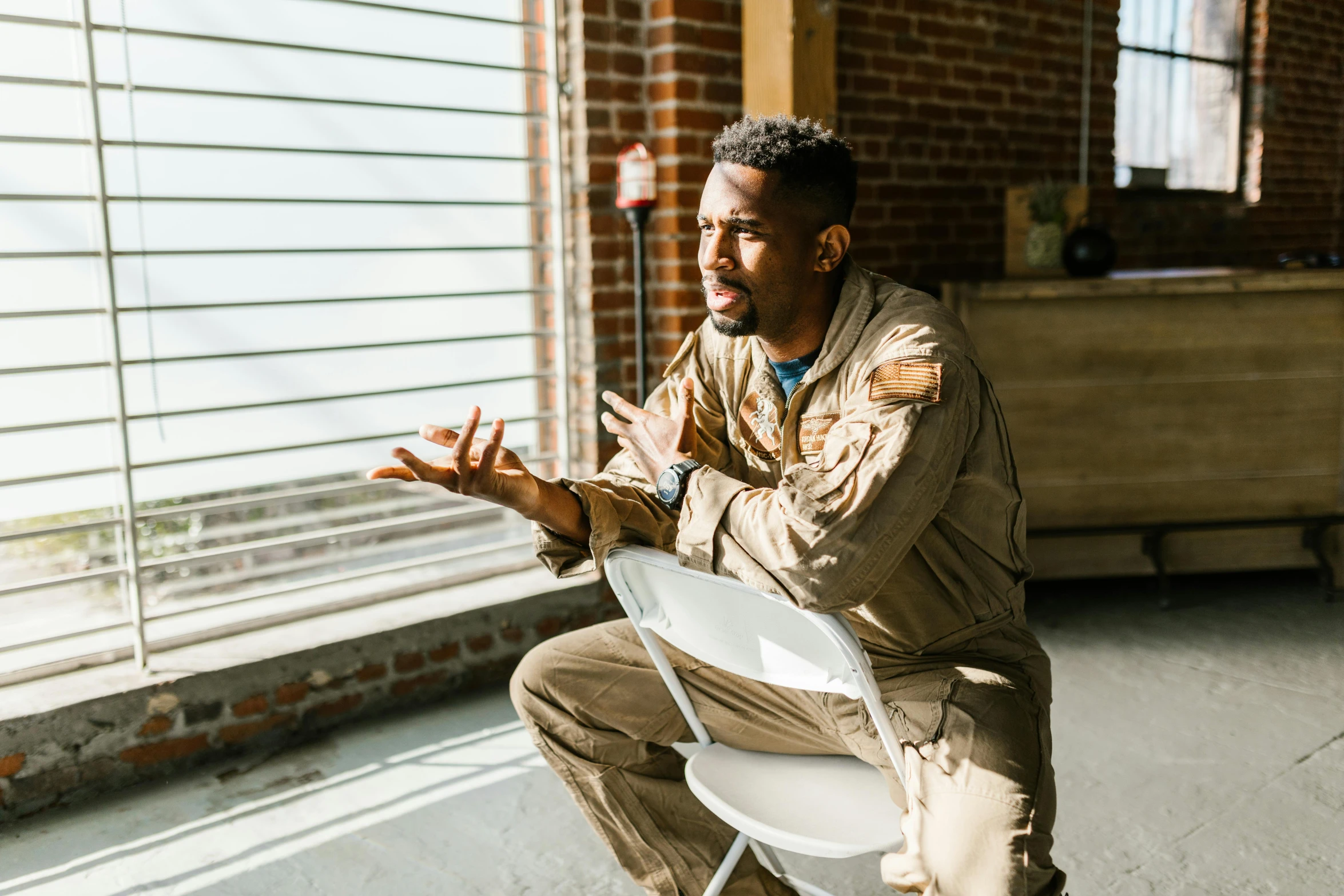a man sitting on a chair in front of a window, pexels contest winner, black arts movement, wearing human air force jumpsuit, telling stories, ( ( theatrical ) ), rugged soldier