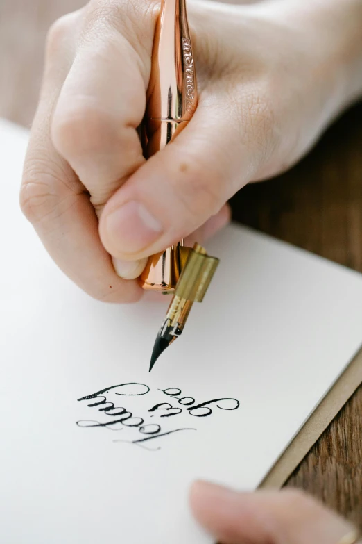 a person writing on a piece of paper with a pen, by Matthias Stom, pexels contest winner, letterism, gold, instagram story, elegant composition, celebrating