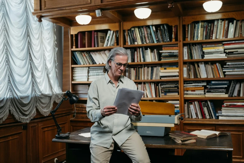 a man sitting at a desk reading a book, by Nina Hamnett, in a museum room, holding books, david cronenberg, profile image