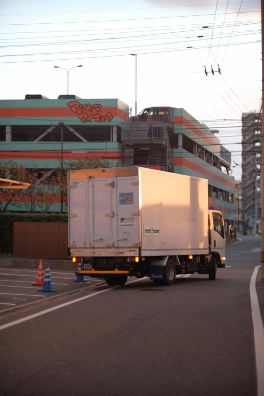 a white truck driving down a street next to a tall building, by Sengai, japan shonan enoshima, low quality photo, cardboard, image