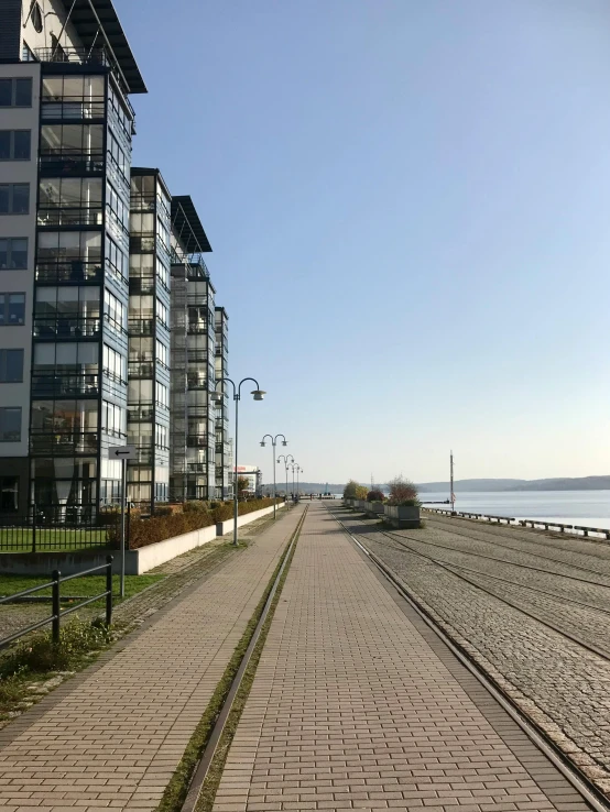 a train traveling down a train track next to tall buildings, next to the sea, espoo, walking to the right, low quality photo