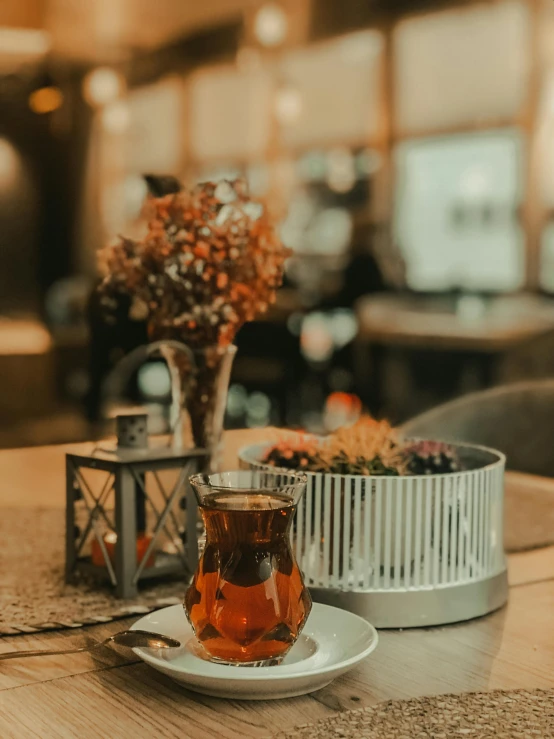 a cup of tea sitting on top of a wooden table, trending on pexels, hurufiyya, a multidimensional cozy tavern, in a short round glass vase, gray and orange colours, islamic