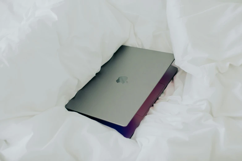 a laptop sitting on top of a bed covered in white sheets, unsplash, apple, glossy surface, wrapped in black, embroidered velvet