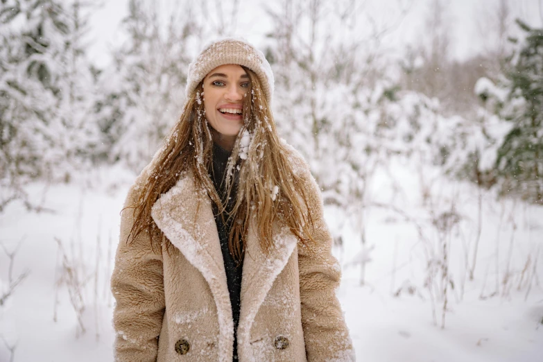 a woman standing outside in the snow, wearing a brown coat and hat