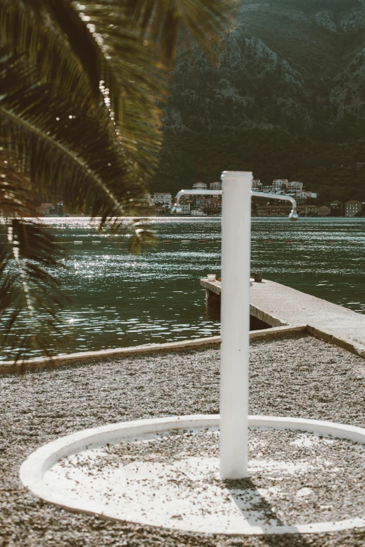 a white umbrella sitting on top of a beach next to a body of water, by Daniel Lieske, trending on unsplash, temporary art, railing along the canal, boka, round base, palm lines