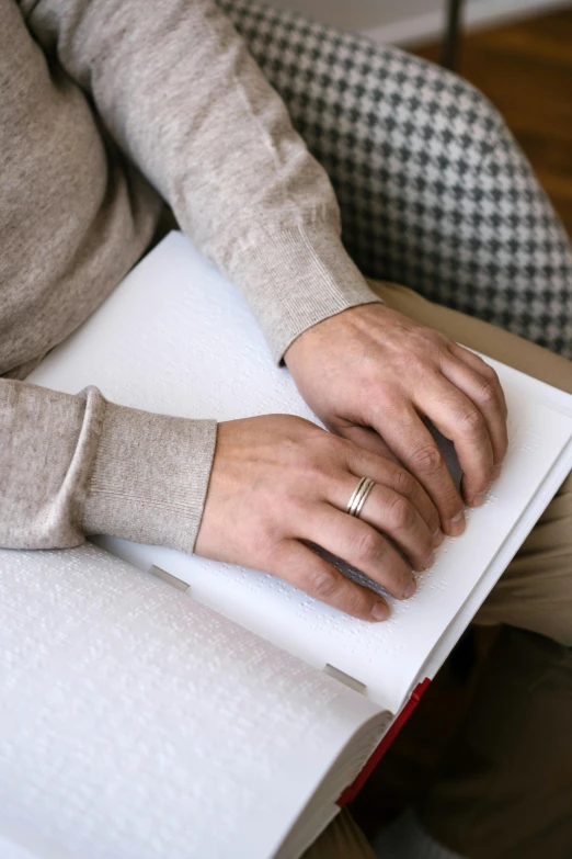 a person sitting on a couch holding a book, by Nina Hamnett, happening, nordic wedding ring, silver，ivory, handcrafted, on high-quality paper