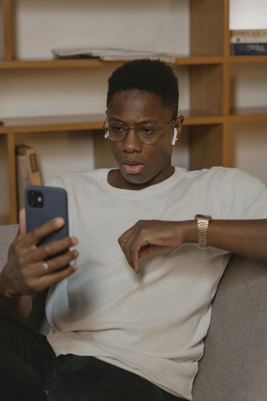 a man sitting on a couch using a cell phone, maria borges, wearing square glasses, lgbtq, tiktok video