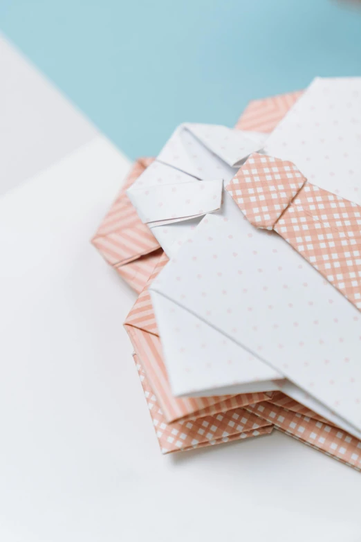 a pile of folded papers sitting on top of a table, wearing a shirt with a tie, nordic pastel colors, repeating pattern, wearing a light - pink suit