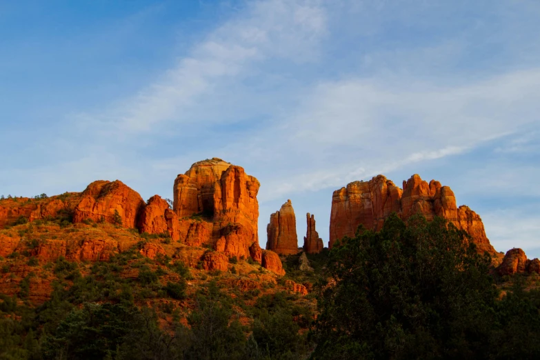 a group of red rocks sitting on top of a lush green hillside, by Linda Sutton, pexels contest winner, hudson river school, chrome cathedrals, godrays at sunset, “ iron bark, saguaro cacti