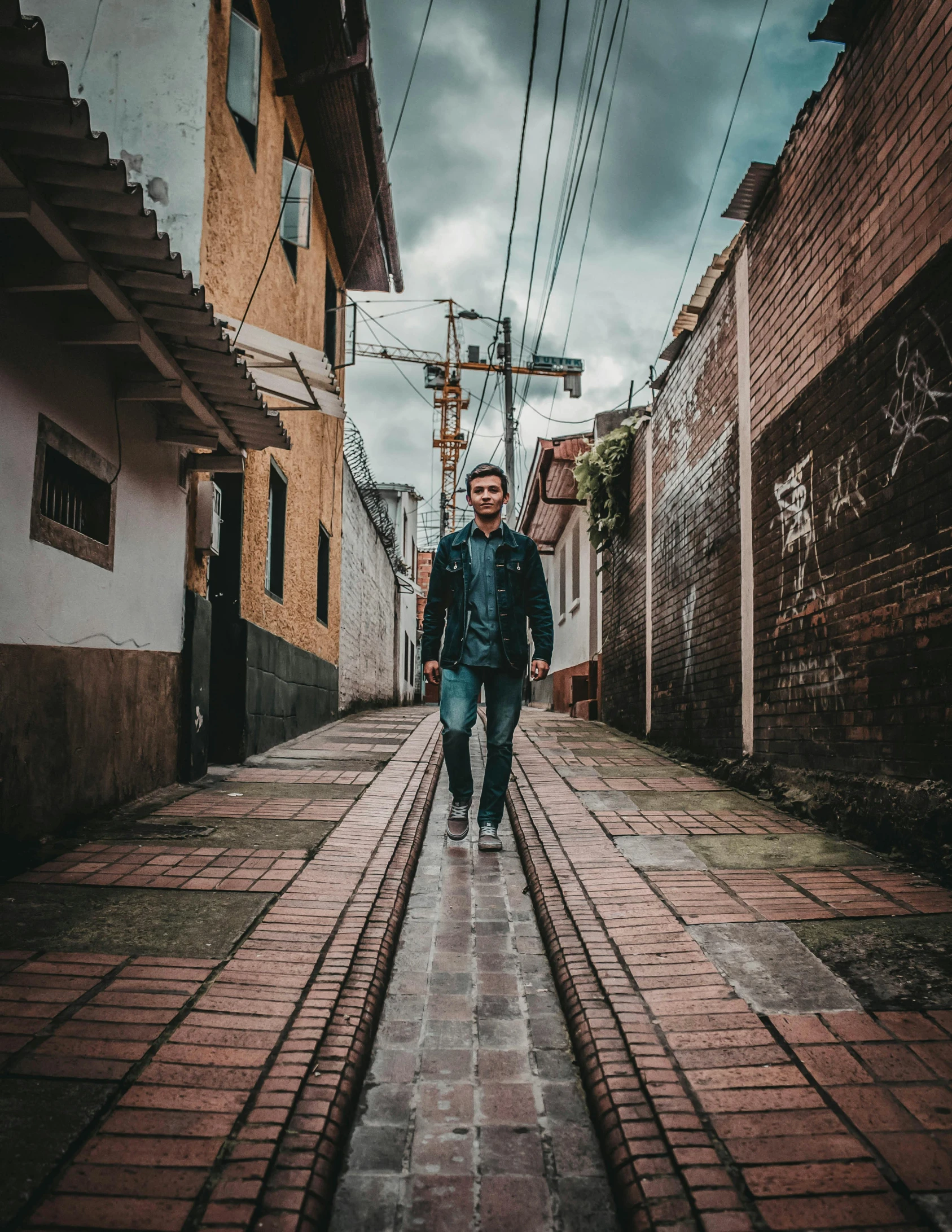 a man walking down a cobblestone street, an album cover, by Alejandro Obregón, pexels contest winner, portrait full body, colombia, leather jacket and denim jeans, neo - andean architecture