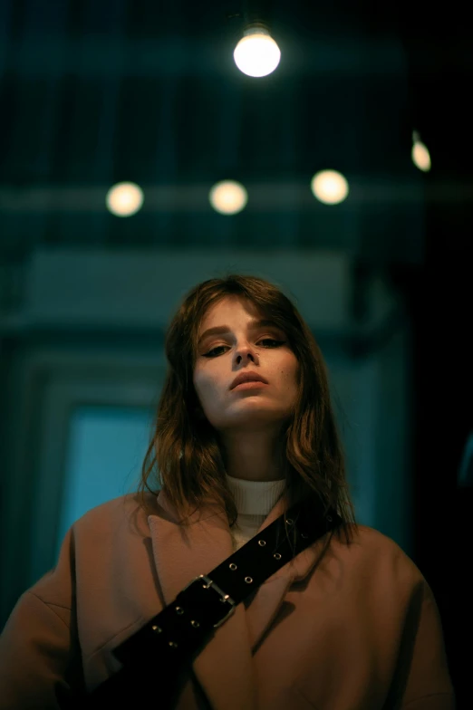 a woman standing in a dimly lit room, an album cover, inspired by Elsa Bleda, trending on pexels, realism, handsome girl, concert, cynthwave, wearing trenchcoat
