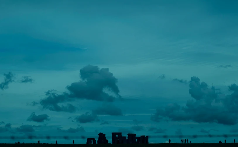 a group of people standing on top of a grass covered field, by Peter Churcher, pexels contest winner, minimalism, with stone henge on top, blue, early evening, aquamarine windows