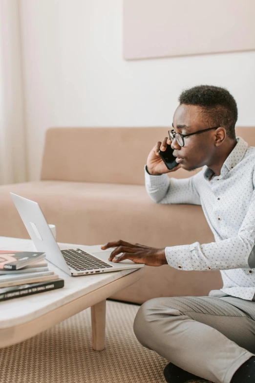 a man sitting on the floor talking on a cell phone, excel running on the computer, black man, selling insurance, using a macbook