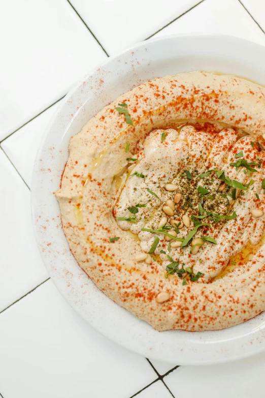 a white plate topped with a bowl of hummusle, by Will Ellis, dau-al-set, humus, hot food, david kassan, light tan