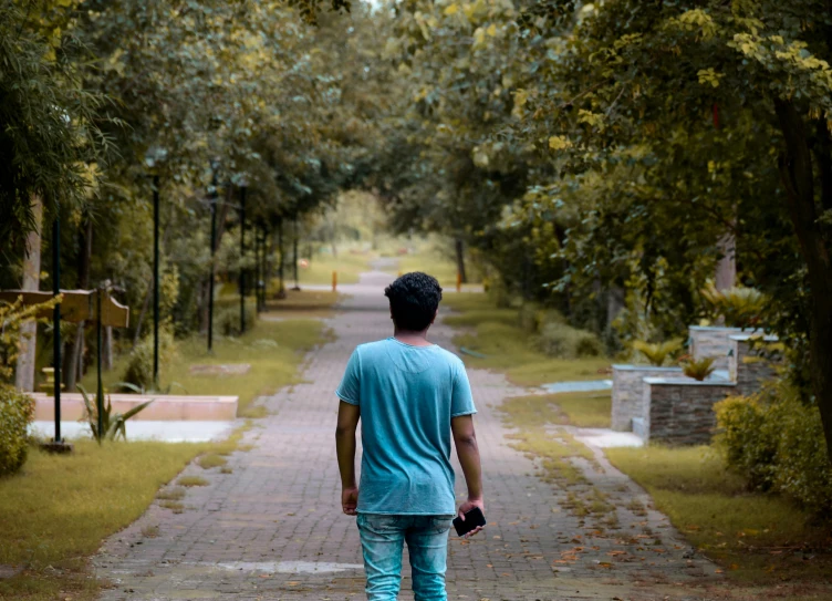 a man walking down a path with a skateboard, a picture, pexels, visual art, sad expression, trees in background, teen boy, street of teal stone