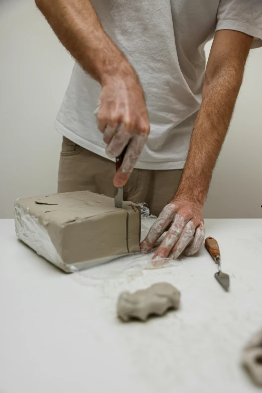 a man that is standing over a table with a knife, a marble sculpture, inspired by Sarah Lucas, process art, white clay, thumbnail, rectangle, pot