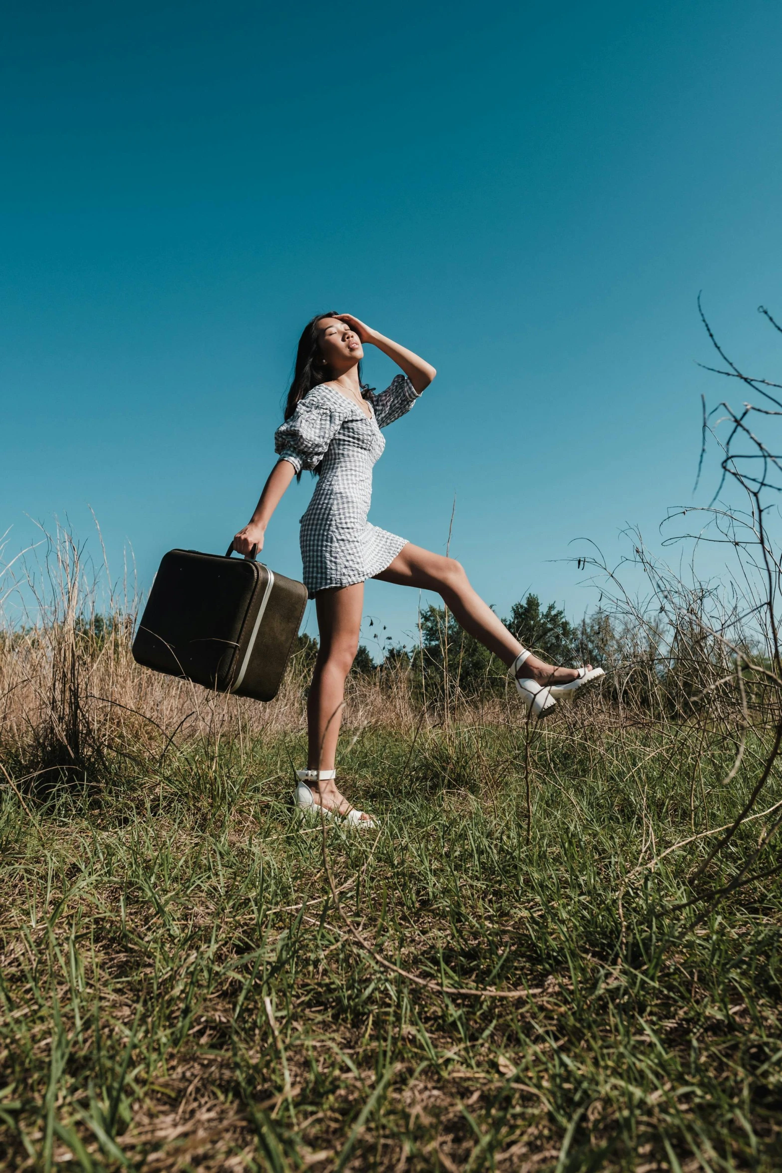 a girl standing in the grass with a suitcase