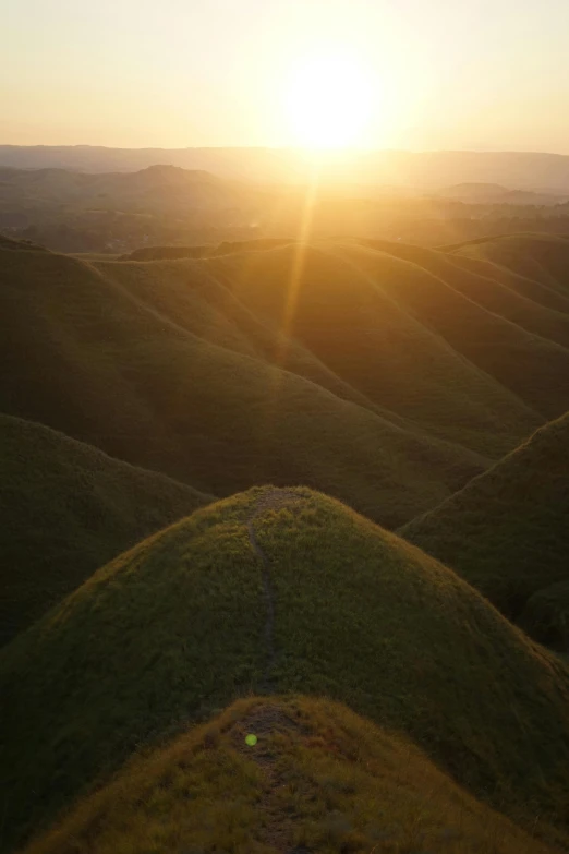 the sun is setting over a grassy hill