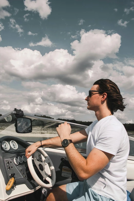 a man sitting in the driver's seat of a boat, inspired by Harry Haenigsen, trending on unsplash, wearing a watch, volume clouds, young man, mid long hair