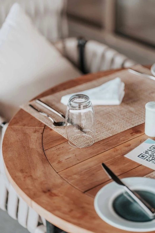 a wooden table topped with a cup of coffee, cutlery, glass jar, sitting on top a table, zoomed in