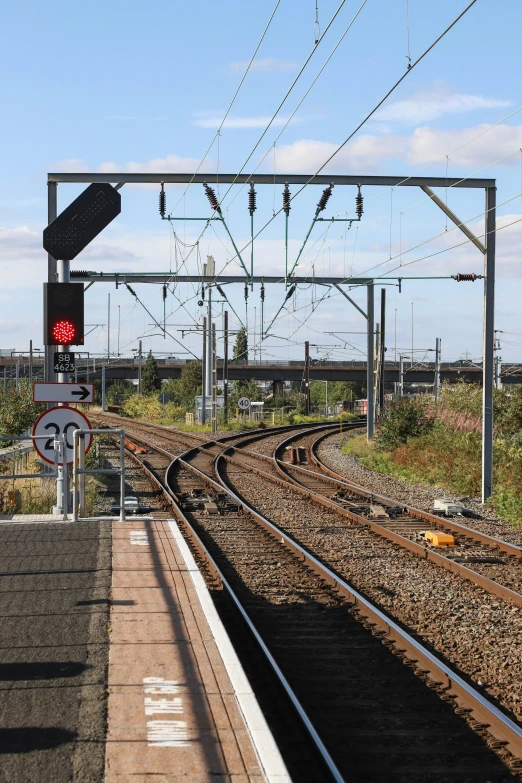 a red traffic light sitting on the side of a train track, telephone wires, seen from a distance, platforms, gateway