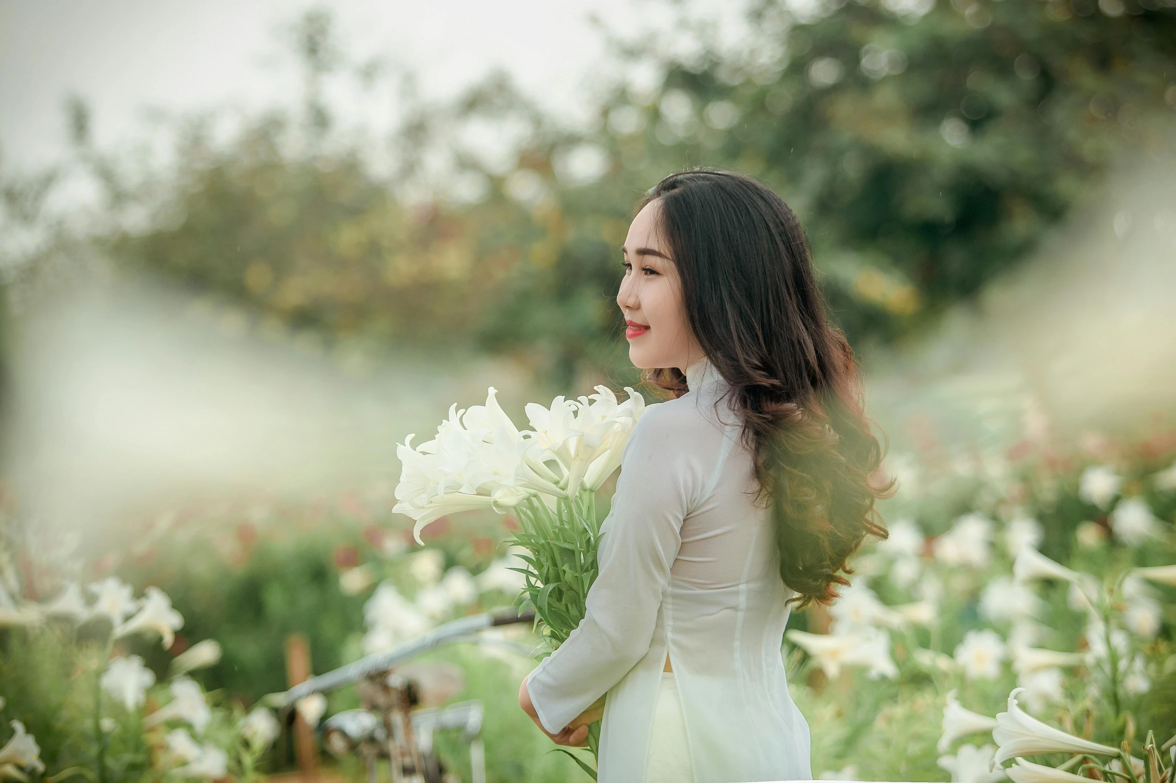 a woman standing in a field of white flowers, by Tan Ting-pho, pexels contest winner, lilies, handsome girl, gardening, white sleeves