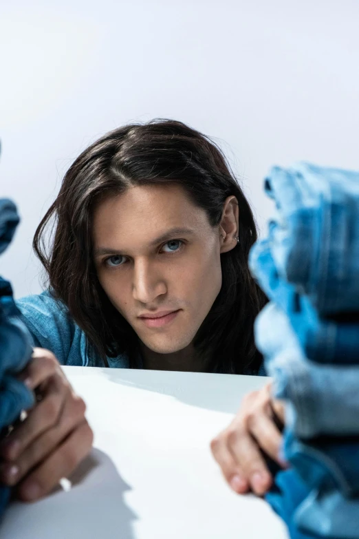 a woman looking at a pile of blue jeans, an album cover, inspired by Jorge Jacinto, trending on reddit, hyperrealism, handsome man, tommy wiseau, nonbinary model, lovingly looking at camera