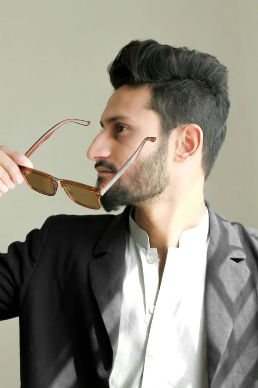 a man holding a pair of glasses in his mouth, an album cover, inspired by Ismail Acar, pexels contest winner, elegant profile pose, brown:-2, reza afshar, spiky