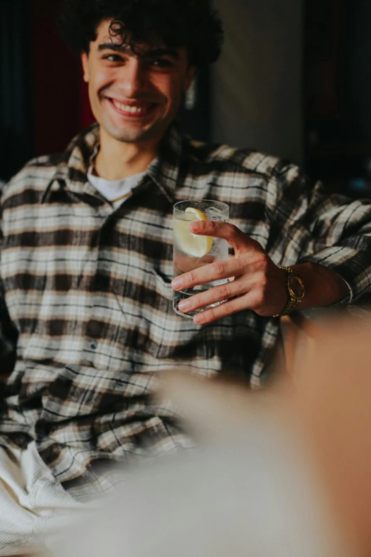 a man sitting at a table with a drink in his hand, pexels contest winner, wearing a plaid shirt, holding a martini, androgynous person, large)}]