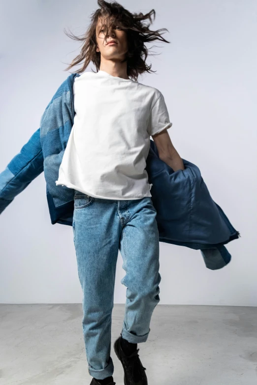 a young man wearing jeans and white t - shirt is carrying a large blue bag