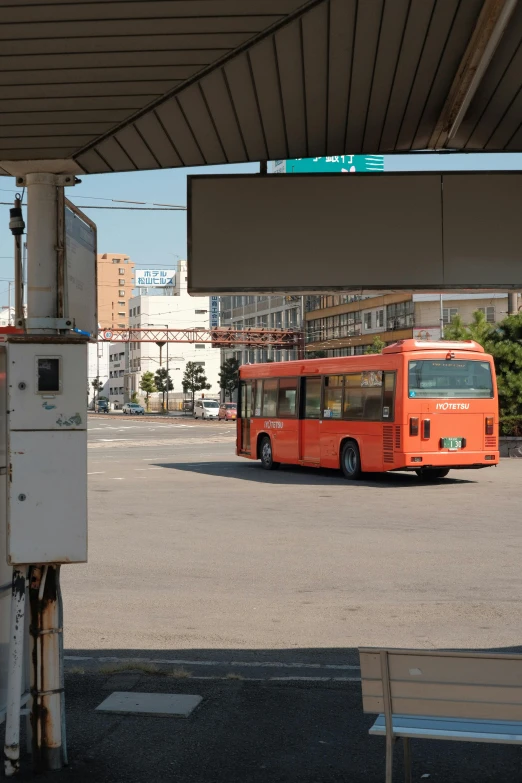 an orange bus parked under a bridge with buildings in the background