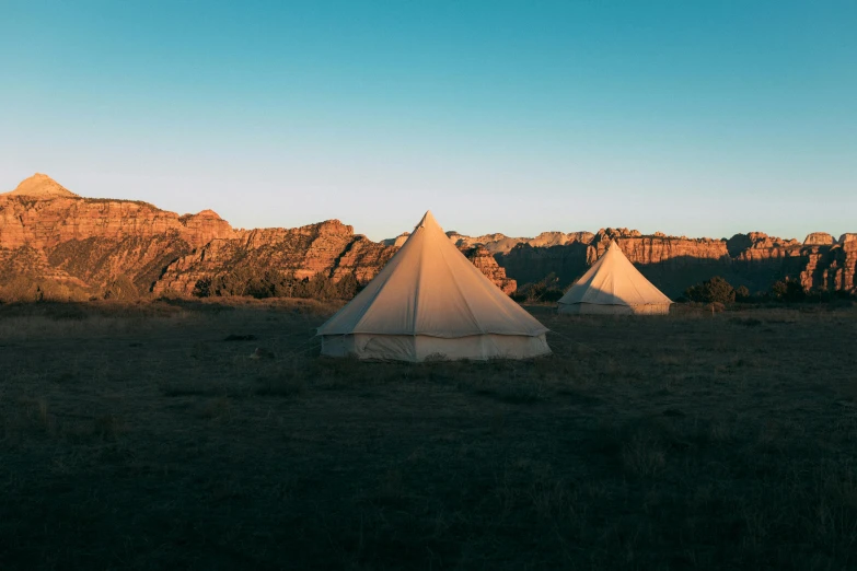 a group of tents sitting on top of a grass covered field, by Lee Loughridge, unsplash contest winner, serene desert setting, ancient interior tent background, warm light, 1 6 x 1 6