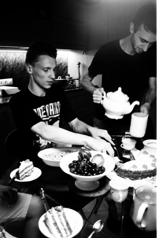 a group of people sitting around a table with plates of food, a black and white photo, tumblr, young tom hiddleston, dmitry prozorov style, tending on arstation, instagram picture