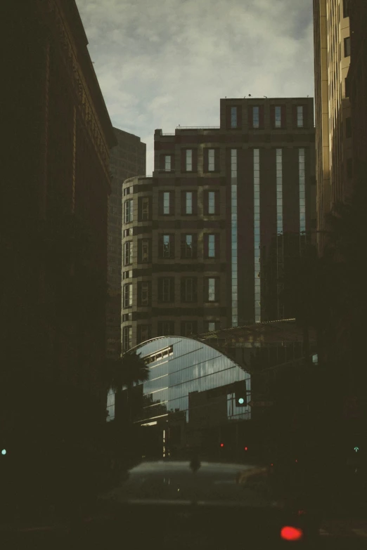 a city street filled with lots of tall buildings, a picture, unsplash contest winner, modernism, faded glow, rounded architecture, dark shadowy surroundings, sunfaded