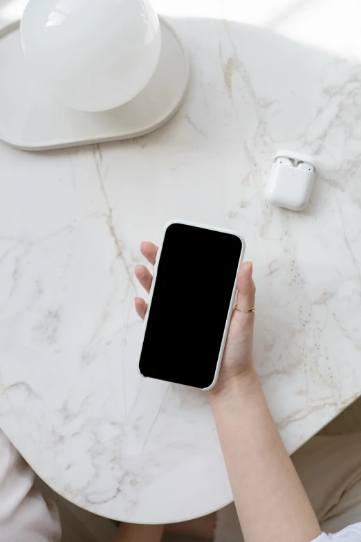 a person sitting at a table with a cell phone in their hand, ivory and black marble, airpods, centered shot, square