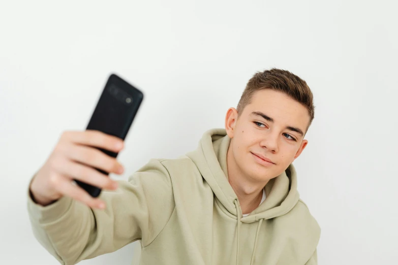 a young man taking a selfie with his cell phone, a picture, trending on pexels, realism, 1 7 - year - old boy thin face, on a pale background, 8 k what, bl