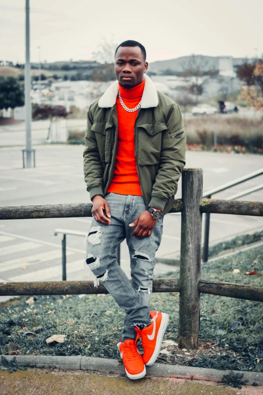 a man standing next to a wooden fence, inspired by Theo Constanté, trending on pexels, orange jacket, young thug, fullbody photo, wearing turtleneck