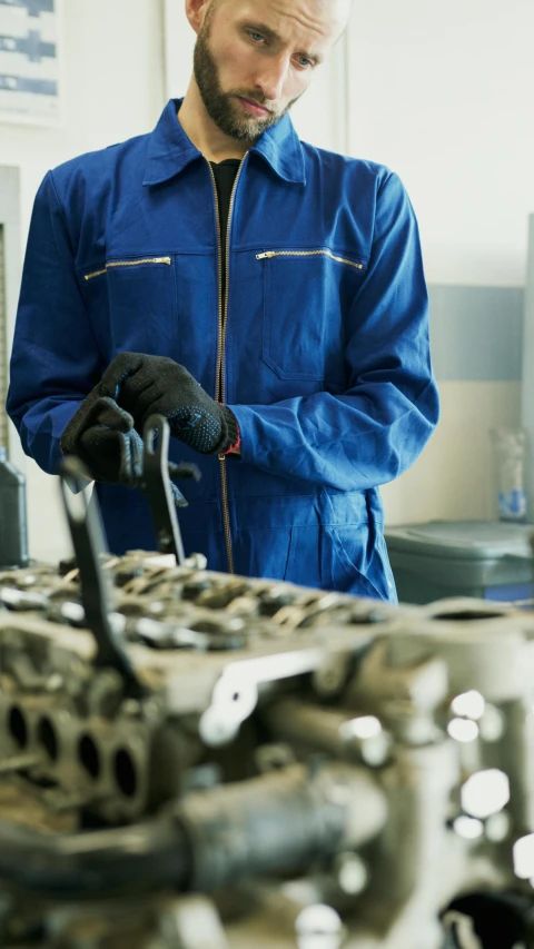 a man working on a car engine in a garage, wearing a blue jacket, digital image, no cropping, thumbnail