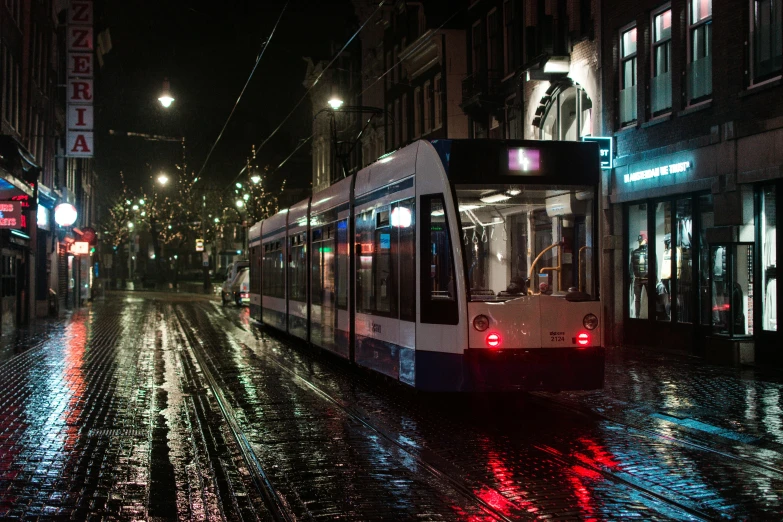 a train traveling down a wet street next to tall buildings, by Jan Tengnagel, unsplash contest winner, street tram, delft, light night, profile image