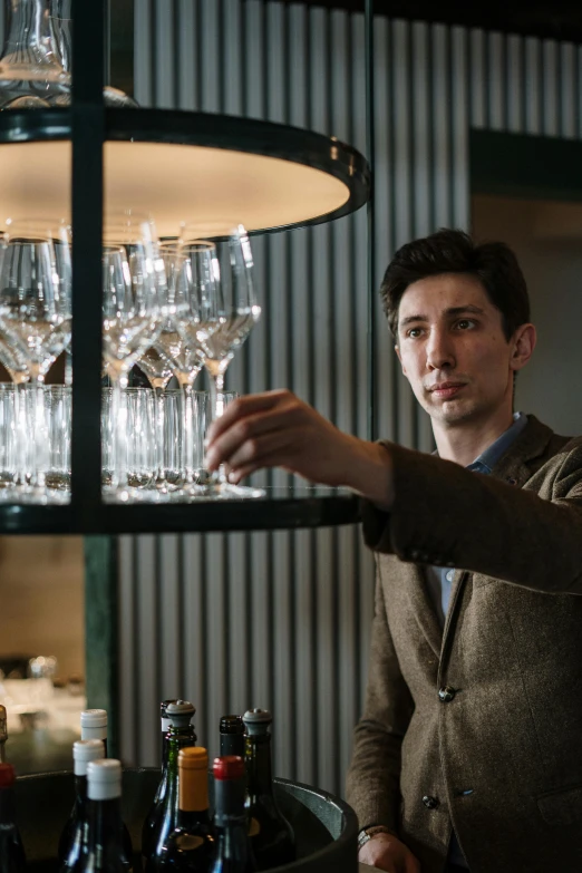 a man standing in front of a shelf filled with wine glasses, mateo dineen, clean lighting, plating, luca