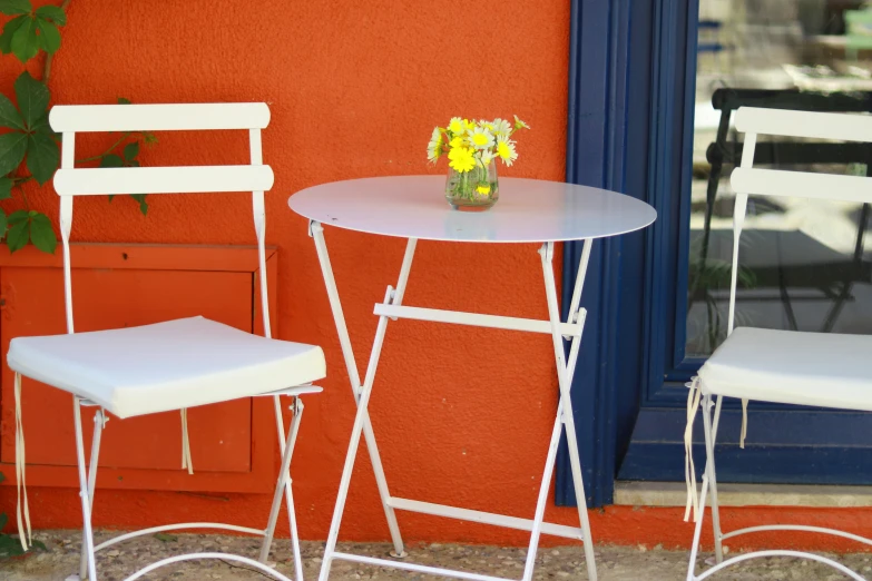 two white metal folding chairs near a table and chair