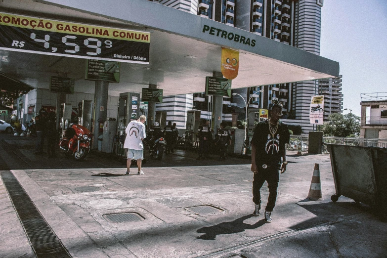 a man standing in front of a gas station, a picture, inspired by Elsa Bleda, pexels contest winner, hyperrealism, playboi carti and lil uzi vert, people walking around, kuala lumpur, medium shot of two characters