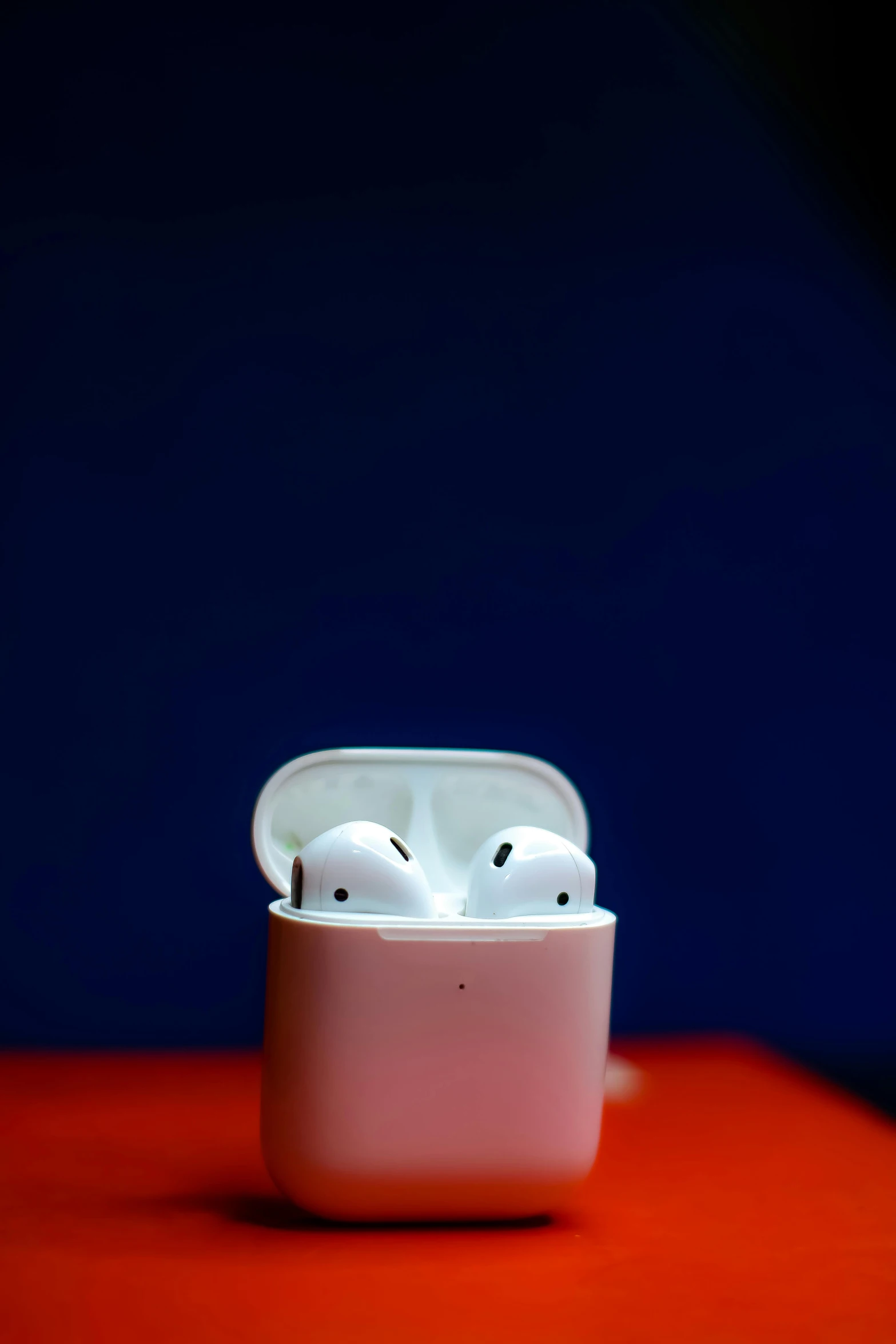 a pair of airpods sitting on top of a red table, by Robbie Trevino, pexels, ap news photo, ox, on display, #oc