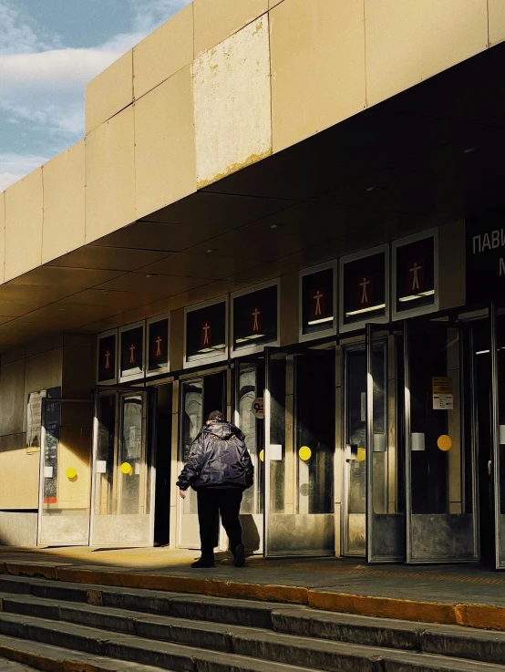 a man that is standing in front of a building, an album cover, by David Palumbo, unsplash, visual art, bus station, [ theatrical ], doors, a woman walking