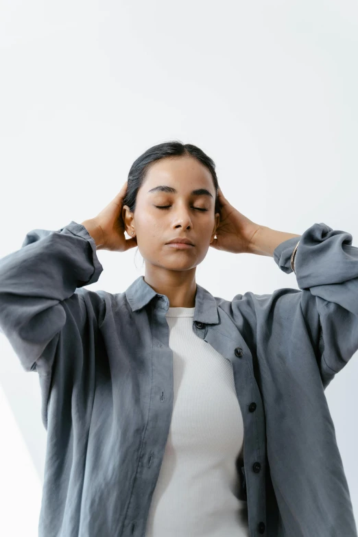 a woman standing with her hands on her head, trending on pexels, renaissance, grey jacket, vibrating, wearing a linen shirt, electrostatic hum