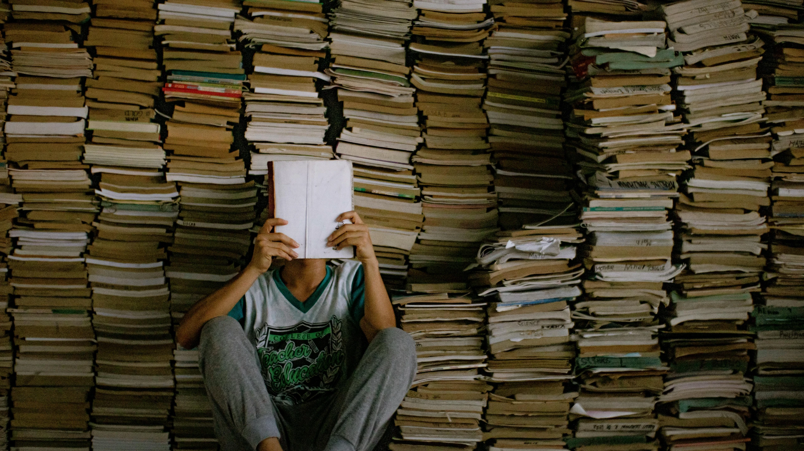 a person sitting in front of a pile of books, pexels contest winner, fungal pages, declassified, it's all in your head, criterion collection