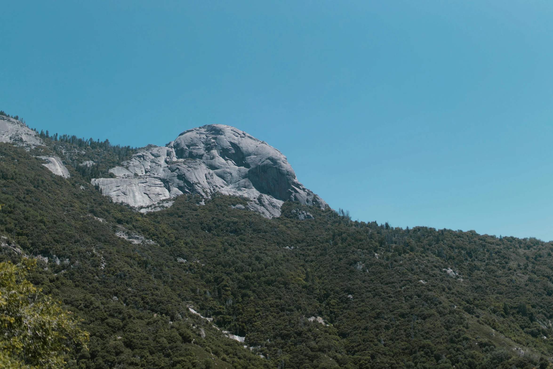 a hill and tree covered side under a blue sky