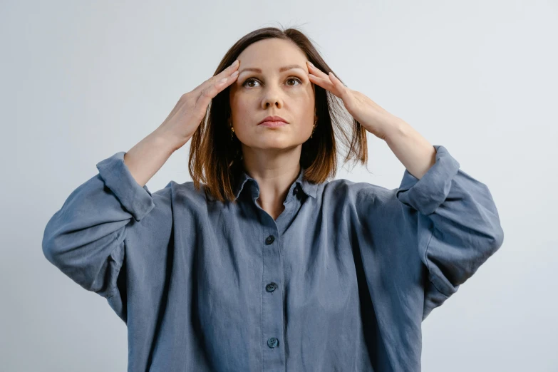 a woman holding her head in front of her eyes, by Anna Füssli, trending on pexels, blue shirt, shrugging, alexey gurylev, overcast