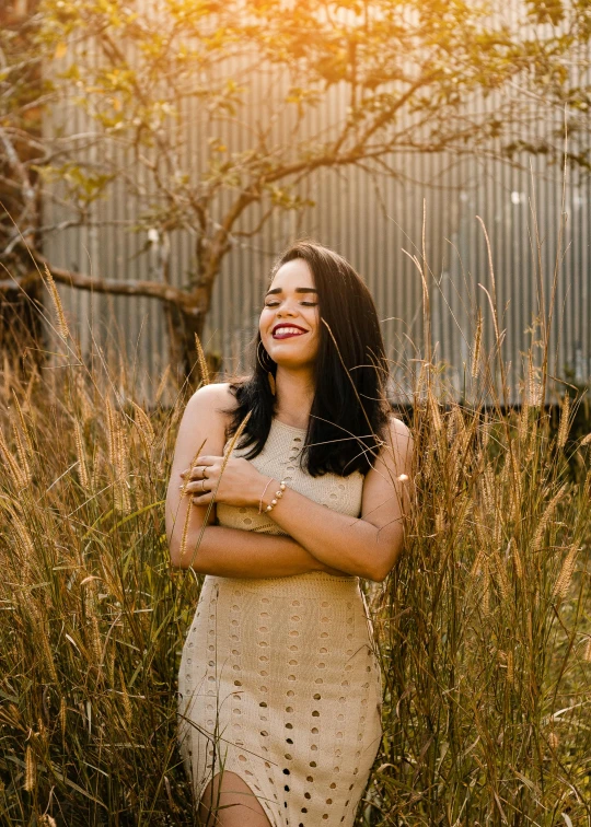 a woman standing in a field of tall grass, by Briana Mora, pexels contest winner, relaxed. gold background, smiling laughing, hispanic, indoor picture