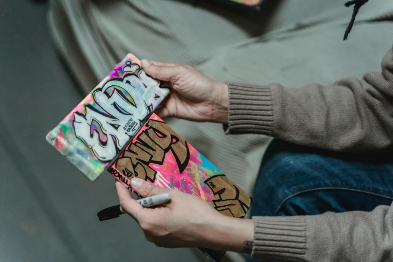 a person sitting on a couch holding a skateboard, an airbrush painting, trending on pexels, graffiti, chocolate candy bar packaging, cell cover style, caligraphy, fully covered in colorful paint
